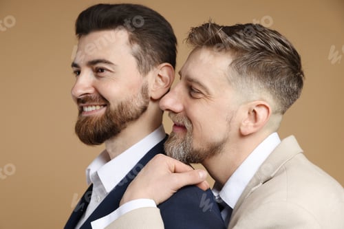 Preview: Happy gay couple in stylish suits on beige background