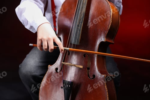 Preview: Little boy playing violoncello on dark red background, closeup