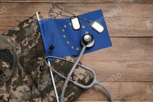 Preview: Stethoscope, flag of European Union, tags and military uniform on wooden table, flat lay. Space for