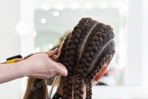 Preview: Hairstylist braiding teenage girl's hair in salon, closeup