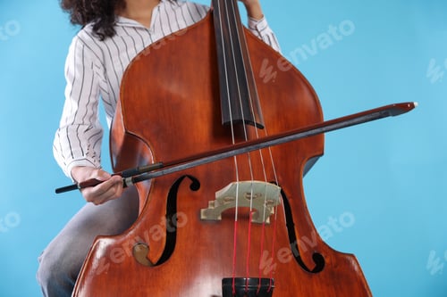 Preview: Woman playing double bass on light blue background, closeup