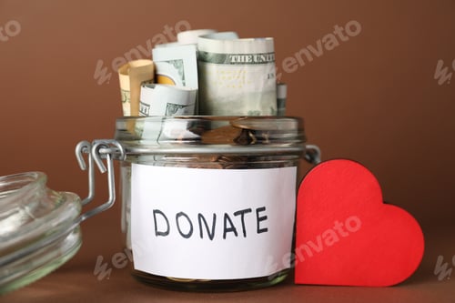Preview: Donation jar with money and red decorative heart on brown background, closeup