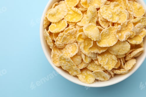 Preview: Tasty corn flakes in bowl on light blue background, top view. Space for text