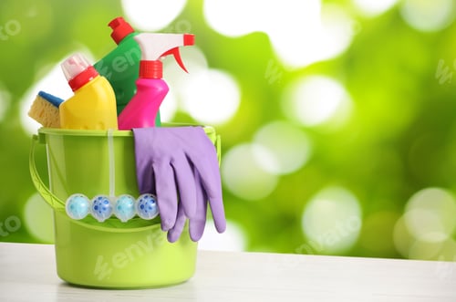 Preview: Spring cleaning time. Bucket with cleaning supplies on table against blurred green background