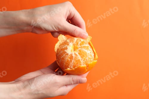 Preview: Woman peeling tangerine on orange background, closeup
