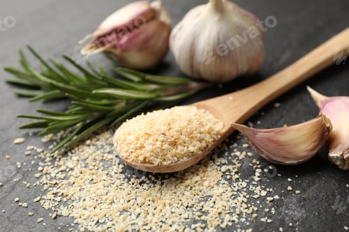 Preview: Granulated dried garlic, spoon, rosemary and fresh vegetables on dark textured table, closeup