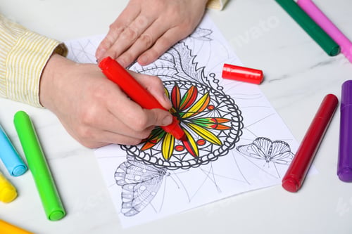 Preview: Woman coloring antistress picture with felt tip pen at white table, closeup