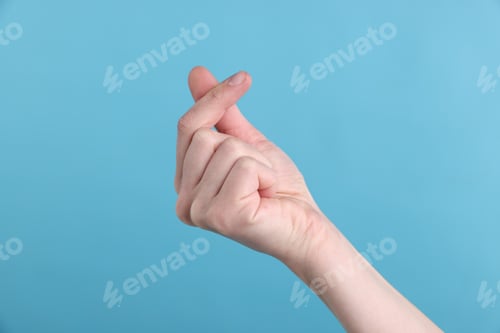 Preview: Woman showing heart gesture with fingers on light blue background, closeup