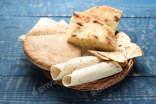 Preview: Tasty pita bread and lavash in wicker basket on blue wooden table, closeup