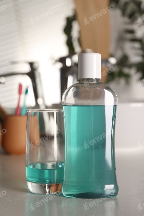 Preview: Bottle and glass of mouthwash on light table in bathroom