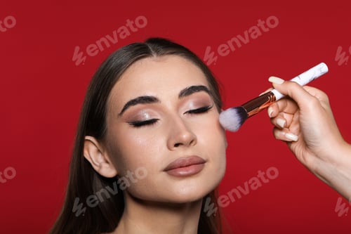 Preview: Artist doing beautiful makeup on woman's face against red background, closeup