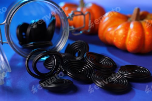 Preview: Overturned jar with natural licorice candies and pumpkins on blue background, selective focus