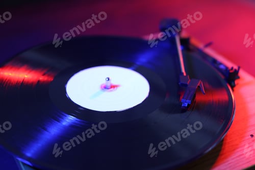 Preview: Modern turntable with vinyl record on table in color lights, closeup