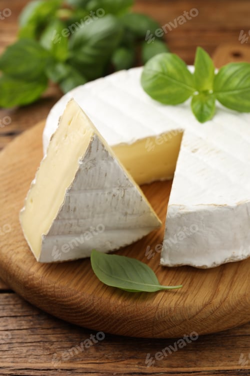 Preview: Cut delicious brie cheese and basil on wooden table, closeup