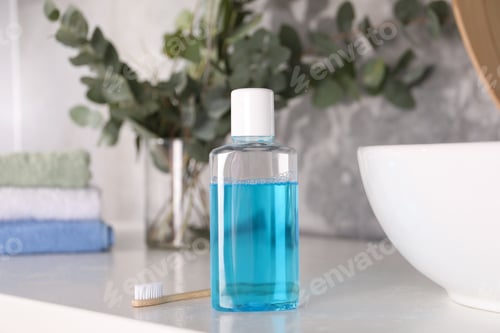 Preview: Bottle of mouthwash and toothbrush on white table in bathroom