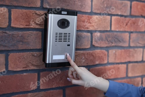 Preview: Woman pressing button on intercom panel near brick wall, closeup
