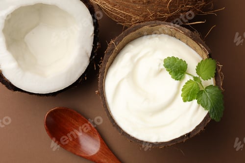 Preview: Tasty coconut yogurt with melissa leaves in shell and nuts on brown background, flat lay