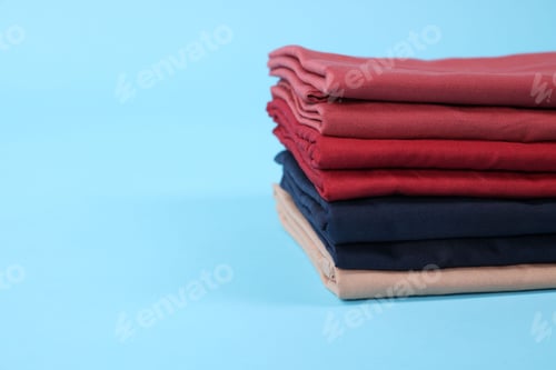 Preview: Stack of colorful bed linens on light blue background, closeup. Space for text