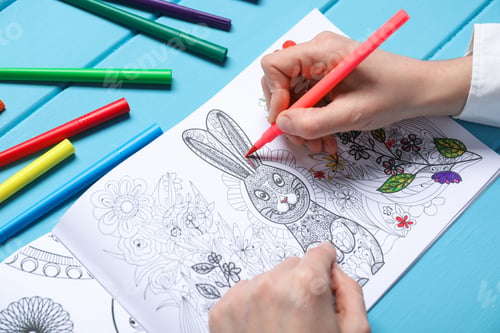 Preview: Woman coloring antistress picture with felt tip pen at light blue wooden table, closeup