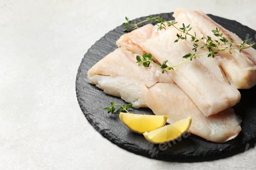 Preview: Pieces of raw cod fish and lemon on light grey table, space for text