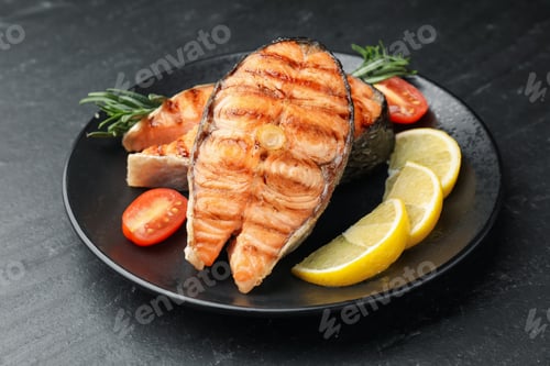 Preview: Tasty grilled salmon steaks served with tomatoes, rosemary lemon on black table, closeup