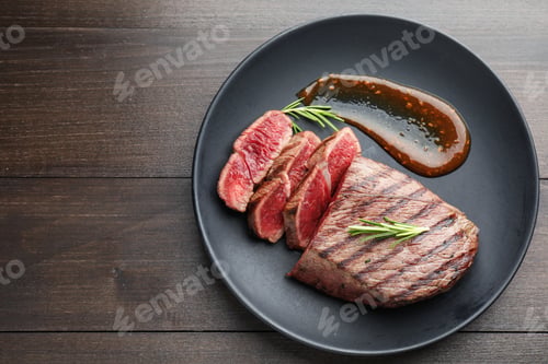 Preview: Pieces of tasty beef steak with rosemary and sauce on wooden table, top view. Space for text