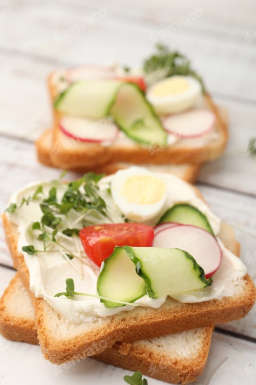 Preview: Tasty sandwiches with cream cheese, microgreens, eggs, tomatoes and cucumbers on light table, closeu