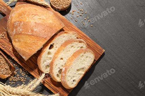 Preview: Cut loaf of fresh bread, spikes and grain on black table, flat lay. Space for text