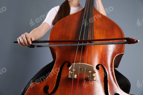 Preview: Girl playing double bass on grey background, closeup
