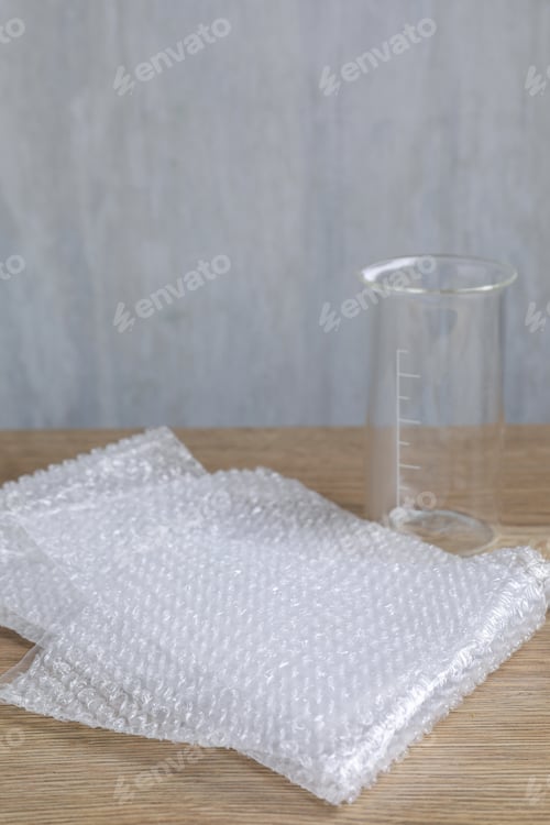 Preview: Bubble wrap and glass beaker on wooden table, closeup