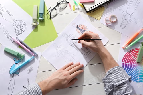 Preview: Fashion designer drawing sketch of outfits at white wooden desk, top view