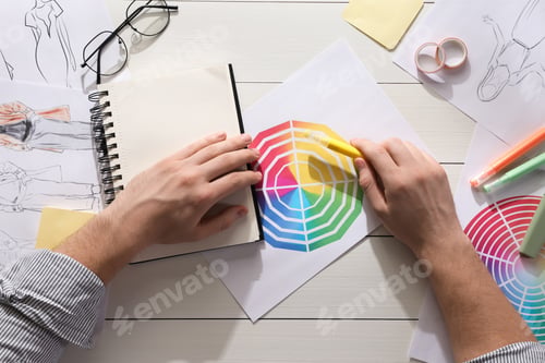 Preview: Fashion designer with color wheel at white wooden desk, top view