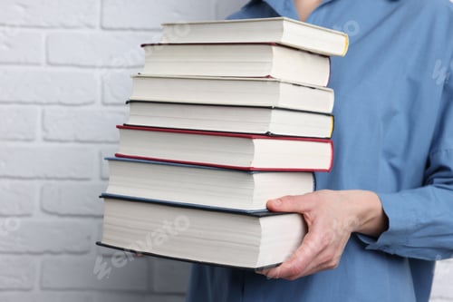 Preview: Woman holding stack of different books near white brick wall, closeup