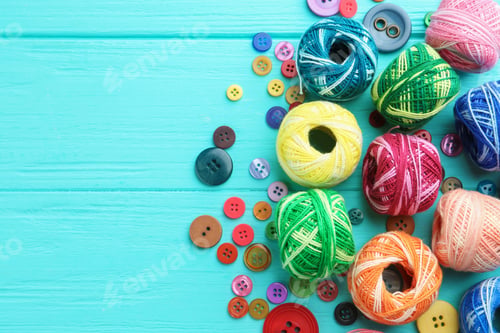 Preview: Balls of bright knitting yarn and buttons on light blue wooden background, flat lay. Space for text