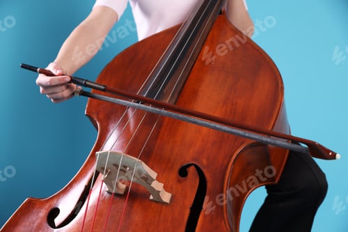 Preview: Girl playing double bass on light blue background, closeup