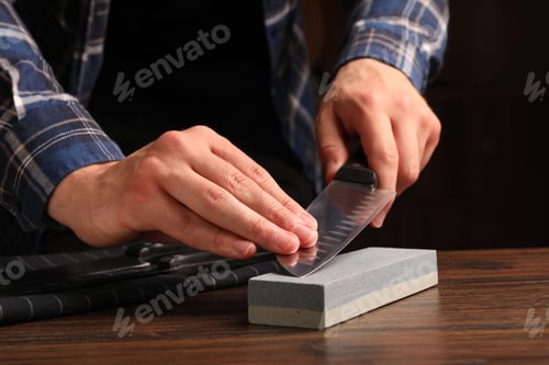 Preview: Man sharpening knife at wooden table, closeup