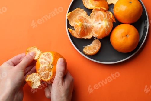 Preview: Woman peeling ripe tangerine and fresh fruits on orange background, top view