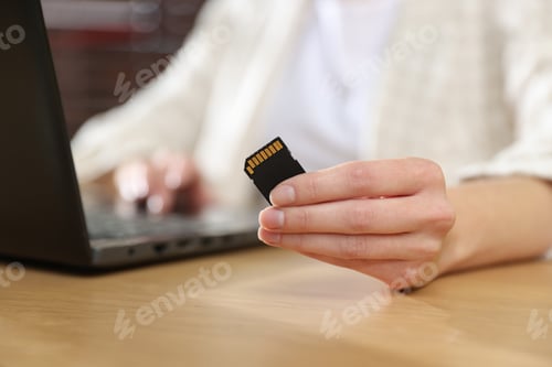 Preview: Woman with SD card working on laptop at desk, closeup