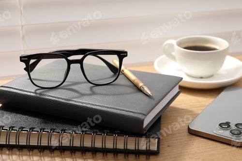 Preview: Pair of stylish glasses, notebooks, smartphone and cup of coffee on wooden table indoors, closeup