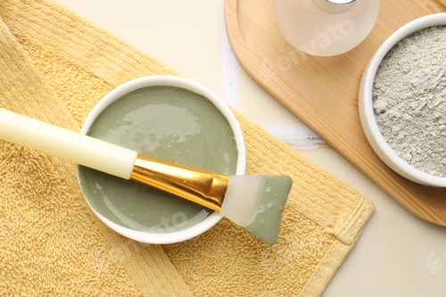 Preview: Clay powder, paste, brush and towel on beige tiled background, flat lay