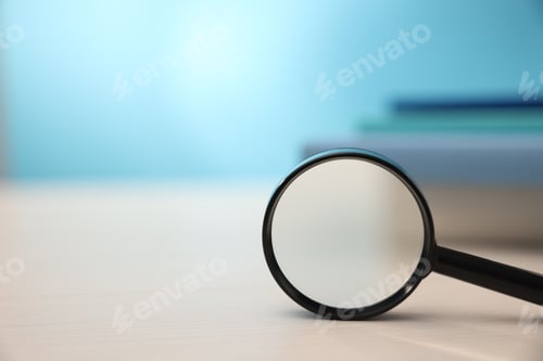 Preview: Magnifying glass and books on wooden table against light blue background, closeup. Space for text