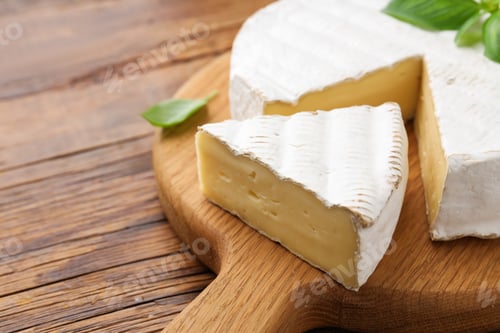 Preview: Cut delicious brie cheese and basil on wooden table, closeup. Space for text