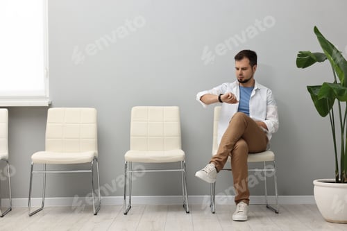 Preview: Man looking at wrist watch and waiting for appointment indoors