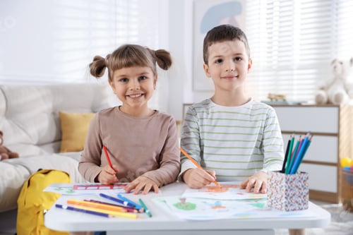 Preview: Little brother and sister drawing together at table indoors