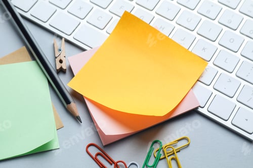 Preview: Reminder. Blank sticky note, pencil, paperclips and keyboard on grey table, closeup