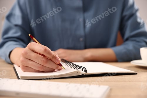 Preview: Woman writing in notebook with pen at table, closeup