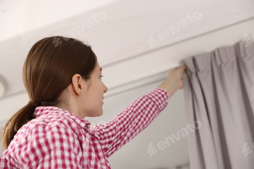 Preview: Woman hanging up window curtains at home, low angle view