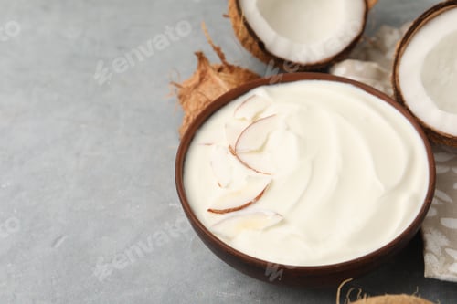 Preview: Delicious coconut yogurt with flakes in bowl and fruits on grey table, closeup. Space for text