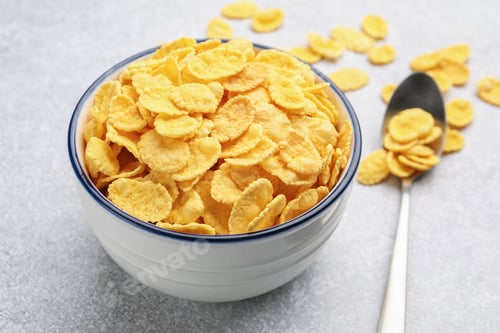 Preview: Tasty corn flakes in bowl and spoon on light grey table, closeup