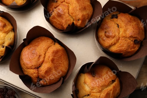 Preview: Tasty muffins with raisins in cupcake tray on table, top view